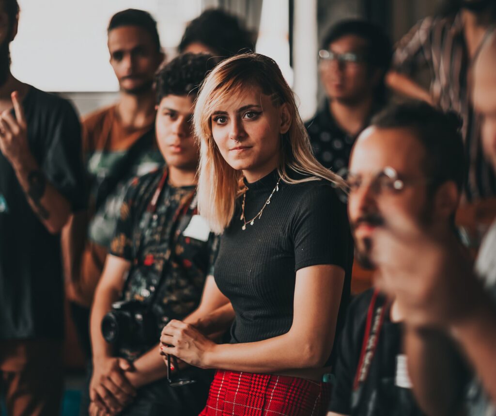 A woman looking ahead wearing a black t-short and red skirt. Other people are in the background but blurred out.